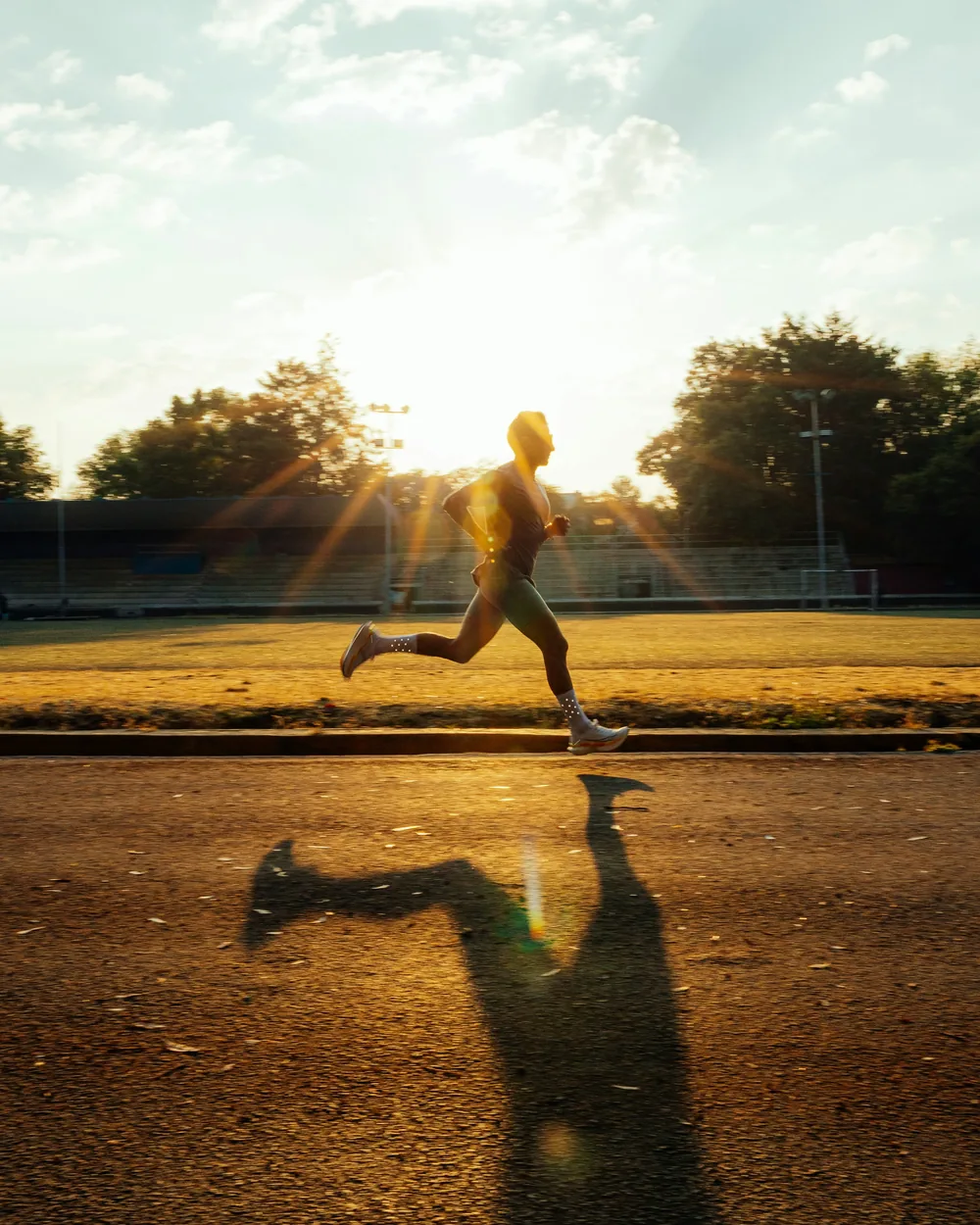 Runner sprinting past a sports field in evening sunlight